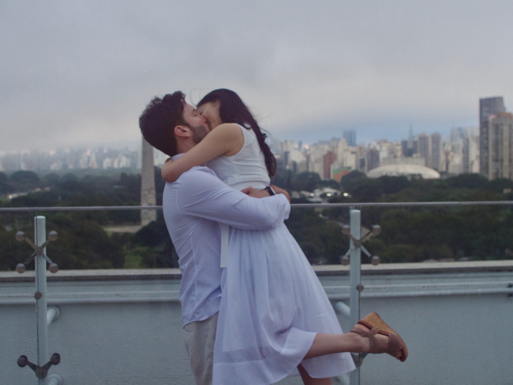 Beto and Marika embracing on a rooftop with the São Paulo skyline behind them